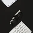 58dac37f-5a32-4133-9387-738f7e332a72-elevated-view-spiral-notepad-eyeglasses-keyboard-black-desk.jpg